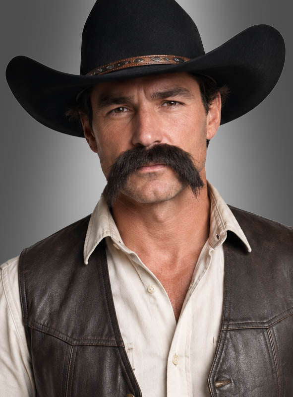 Ein Mann mit schwarzem Cowboyhut, einem dichten Beeindruckender Schnauzer Bart, weißem Hemd und brauner Lederweste, der mit ausdruckslosem Blick in die Kamera blickt, vor einem grauen Hintergrund – ein echter Cowboy-Bart-Style, ideal für Fans des Beeindruckender Schnauzer Bart für Herren-Looks.