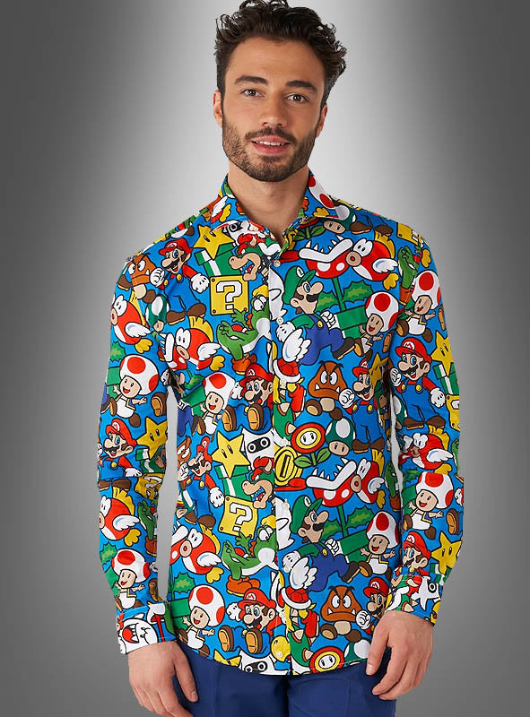 Ein Mann, der das „Super Mario Hemd“ von OppoSuits trägt – ein farbenfrohes Hemd mit Knöpfen, das mit Super-Mario-Figuren und -Symbolen bedruckt ist –, steht vor einem grauen Hintergrund mit Farbverlauf.