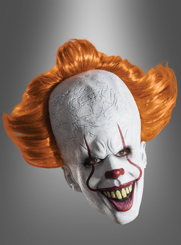 Eine Pennywise-Maske – ein Horrorclown mit übertriebenem Clown-Make-up, leuchtend rotem Haar und bedrohlichen, scharfen Zähnen – ist vor einem grauen Hintergrund mit Farbverlauf abgebildet und bildet so ein gruseliges Halloween-Kostüm-Accessoire, das perfekt für jeden Horrorfan ist.