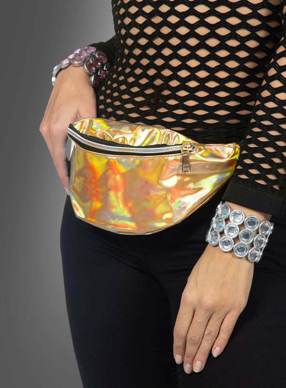 Eine Person, die ein schwarzes Netzoberteil, eine schwarze Hose, klobige Silberarmbänder und die metallisch-goldene Gürteltasche „Schillernde Bauchtasche im Bling-Style“ trägt, vor einem grauen Hintergrund.