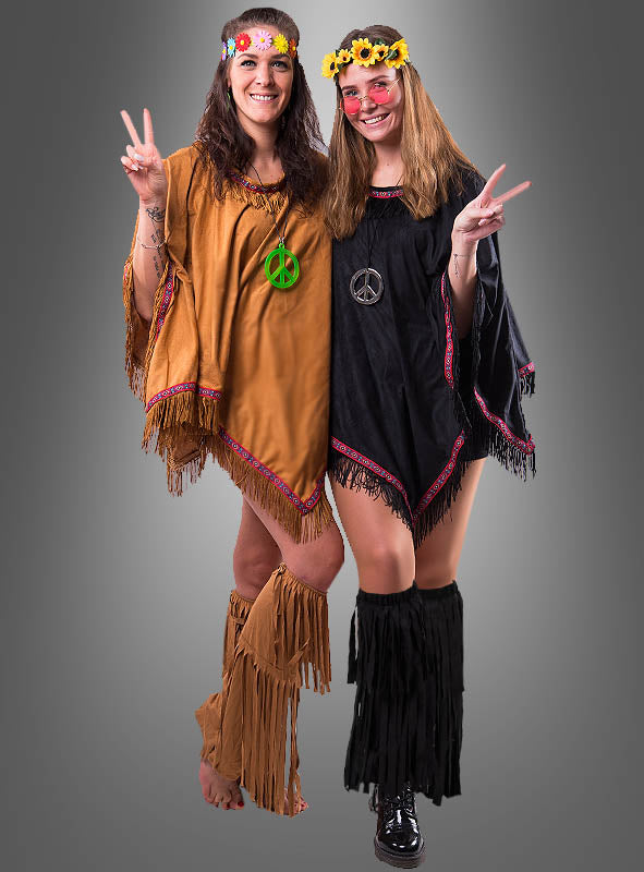 Zwei Frauen in Hippie-Outfits mit Fransen, Blumenkränzen und Halsketten mit Peace-Zeichen tragen jeweils bunte Hippie-Stulpen mit Fransen. Lächelnd und mit erhobenen Peace-Zeichen stehen sie vor einem schlichten grauen Hintergrund.