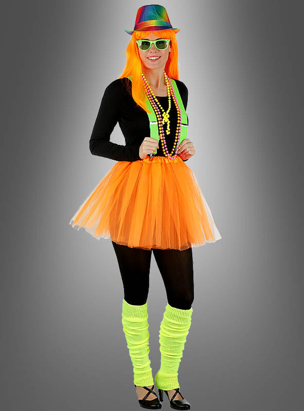 Vor einem grauen Hintergrund steht eine Person, die einen neonfarbenen Regenbogenhut, eine orangefarbene Perücke, ein schwarzes Oberteil, einen orangefarbenen Tutu-Rock, neonfarbene Hosenträger, bunte Perlen, schwarze Leggings und neongelbe Stulpen trägt – abgerundet durch eine auffällige Sonnenbrille „Party Brille“ in verschiedenen Farben. Dieser farbenfrohe Look ist das perfekte Neonparty-Accessoire für jede festliche Feier.