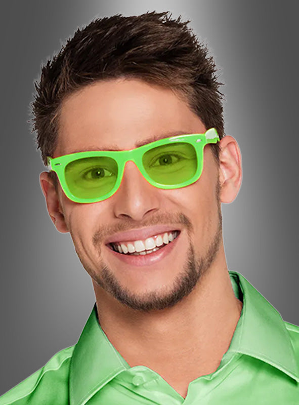 Ein Mann mit kurzen braunen Haaren trägt eine neongrüne „Party Brille“ in verschiedenen Farben sowie ein glänzendes hellgrünes Hemd mit Kragen und lächelt vor einem grauen Hintergrund mit Farbverlauf – damit ist sie das perfekte Neonparty-Accessoire für deine nächste Veranstaltung.