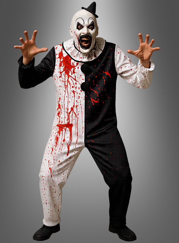 Eine Person, die das Kostüm „Blutiger Horrorclown – Erwachsene“ trägt – ein schwarz-weißes Design mit einer furchterregenden Maske und künstlichen Blutflecken –, posiert bedrohlich mit erhobenen Armen und gespreizten Fingern vor einem grauen Hintergrund.