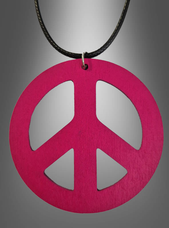 Eine 70er-Jahre-Friedenskette (6,50 cm) aus Holz in Rosa, ideal als Holzamulett für dein Hippie-Kostüm, hängt an einer schwarzen Kordel vor einem grauen Farbverlaufshintergrund.