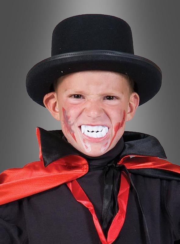 Ein Kind mit schwarzem Zylinder, rot-schwarzem Umhang, einem Vampirgebiss für Kinder und blutähnlichem Make-up, das mit grimmigem Gesichtsausdruck vor einem grauen Hintergrund posiert – das perfekte Accessoire, um jedes Kinder-Vampir-Kostüm für Halloween-Spaß abzurunden.