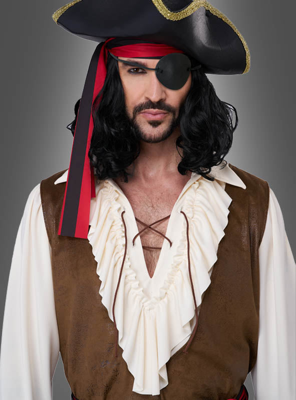 Vor einem grauen Hintergrund steht ein Mann, der eine Piratenverkleidung für Herren trägt, bestehend aus einem schwarzen Hut, einem roten Bandana, einer Augenklappe, einer langen schwarzen Perücke, einem weißen Hemd mit Rüschen und einer braunen Weste.