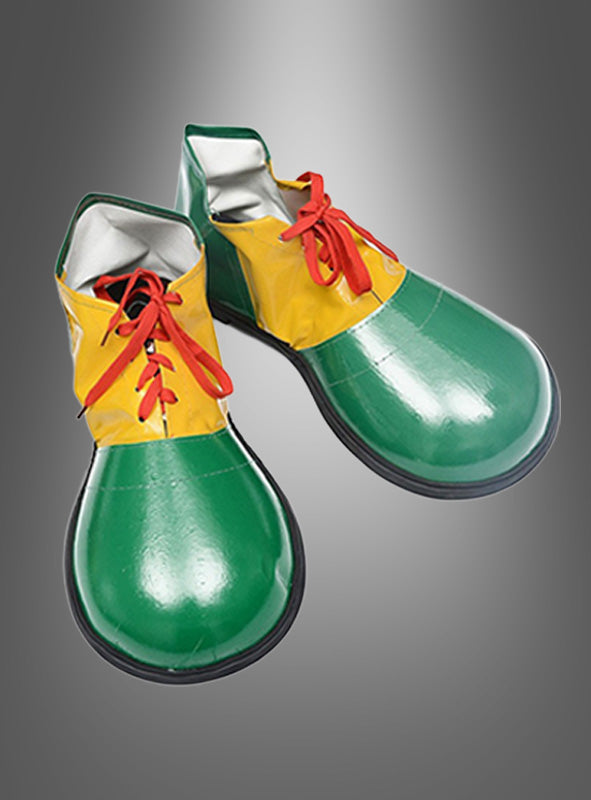 Ein Paar Clown-Schuhe für Erwachsene im Oversize-Design mit grünen Schuhspitzen, gelben Seiten und roten Schnürsenkeln ist vor einem grauen Hintergrund mit Farbverlauf abgebildet.
