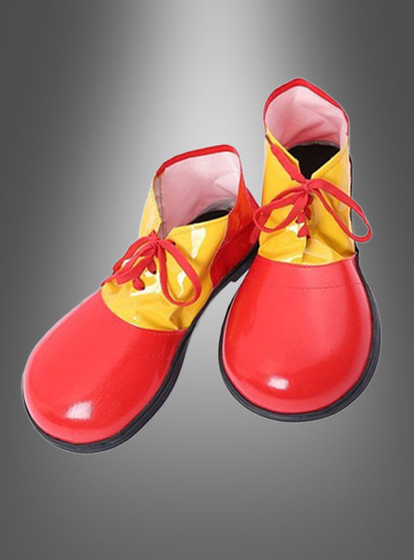 Ein Paar Clownschuhe für Erwachsene mit überdimensionalen, bunten Mustern, glänzenden roten Schuhspitzen, gelbem Obermaterial, roten Schnürsenkeln und schwarzen Sohlen wird vor einem grau verlaufenden Hintergrund präsentiert – ein ideales Accessoire, um jedes Clownskostüm zu vervollständigen.