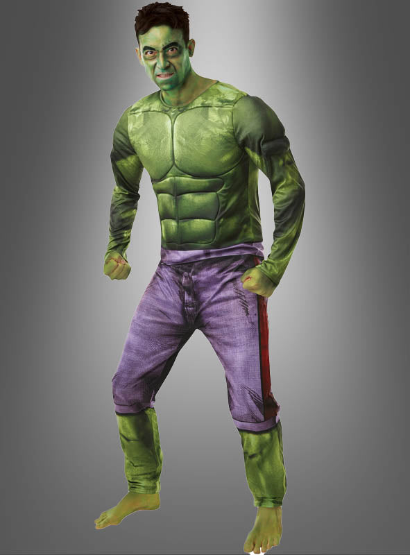 Eine Person, die das „Hulk-Kostüm für Herren von Marvel“ trägt – bestehend aus einem grünen Muskelanzug und einer violetten Hose –, posiert barfuß als Hulk vor einem schlichten Hintergrund mit Farbverlauf.
