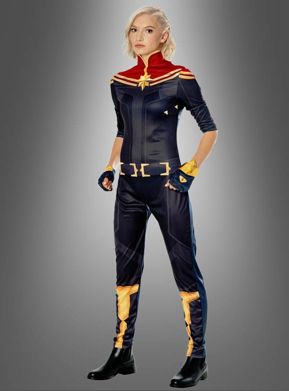 Eine Person steht vor einem grauen Hintergrund und trägt das Captain-Marvel-Kostüm für Damen, das sich durch auffällige rote, blaue und goldene Farben auszeichnet, dazu schwarze Stiefel und kurzes blondes Haar – ein kraftvolles Marvel-Superheldinnen-Kostüm für Damen, das vom Kostüm-Ensemble der Avengers inspiriert ist.