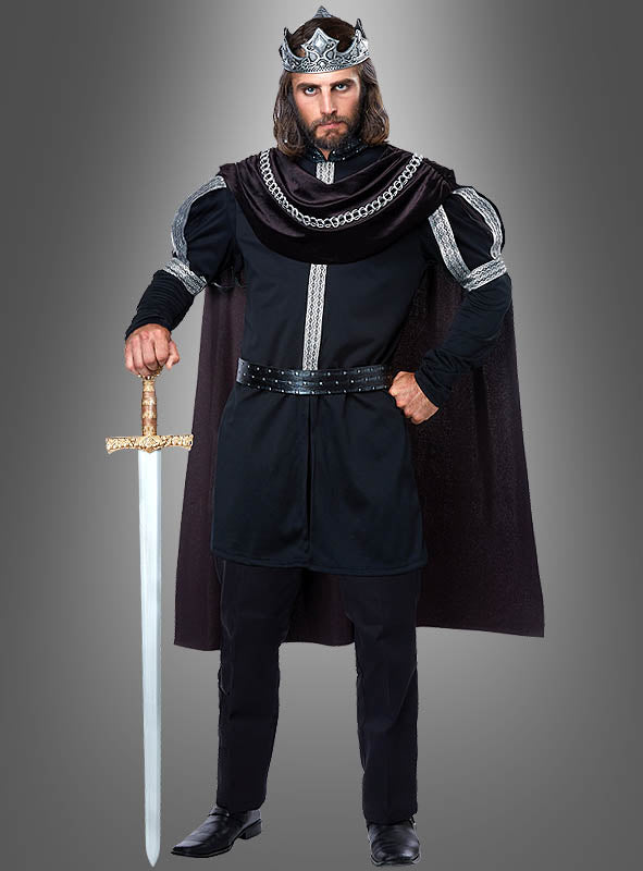 Vor einem grauen Hintergrund steht ein Mann, der eine silberne Krone, einen schwarzen Umhang und das mittelalterliche Kostüm „König Kostüm schwarz für Herren“ trägt und ein nach unten gerichtetes Schwert in der Hand hält.