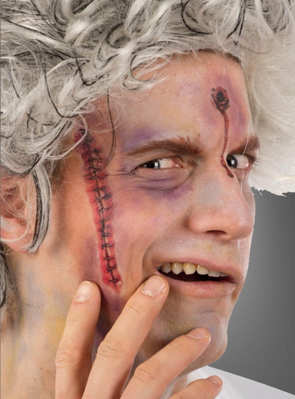 Ein Mann mit weißem, zerzaustem Haar und theatralischem Make-up – darunter eine genähte Narbe auf der Wange und eine künstliche Wunde auf der Stirn, die mit „Blutige Narben Tattoo Wunden“ gestaltet wurde – berührt mit besorgtem Gesichtsausdruck sein Gesicht.