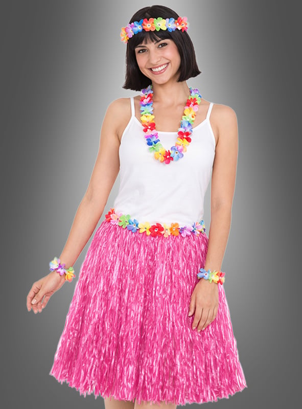 Eine Frau, die ein weißes Trägertop, einen rosa Grasrock und bunte Blumenaccessoires aus dem 5-teiligen Hawaii-Set mit Rock & Accessoires trägt, steht lächelnd vor einem grauen Hintergrund.