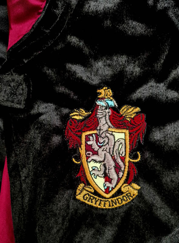 Nahaufnahme eines Gryffindor-Wappenaufnähers auf dunklem Stoff, der beim „Harry Potter Kostüm Gryffindor Deluxe“ zu sehen ist – einer authentischen Robe mit einem Löwenwappen und dem in Goldbuchstaben geschriebenen Hausnamen, perfekt für jedes Harry-Potter-Kostüm.