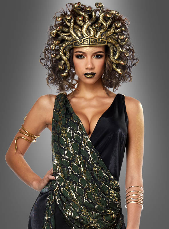 Eine Frau posiert vor einem grauen Hintergrund und trägt das „Medusa Schlangenkostüm für Damen“, das sich durch einen auffälligen Kopfschmuck mit Schlangenmotiv, elegante goldene Accessoires sowie ein schwarz-grünes Ensemble auszeichnet.