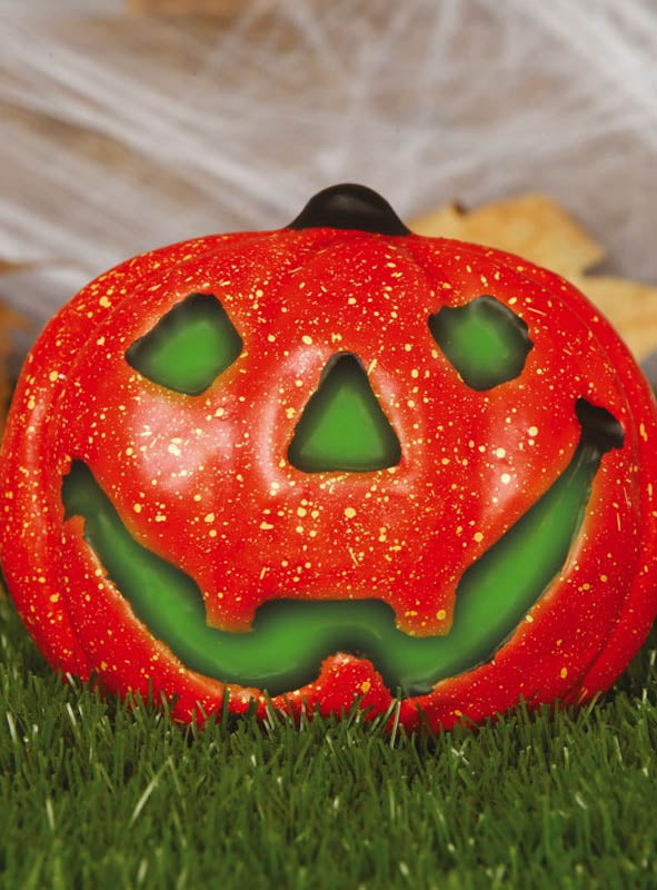 Eine auffällige Halloween-Dekoration mit einem roten Kürbislaternen, der von grünem Licht beleuchtet wird, steht auf dem Rasen vor einem verschwommenen Hintergrund aus Blättern und Spinnweben – damit ist sie die perfekte Wahl für Ihre Halloween-Dekoration.