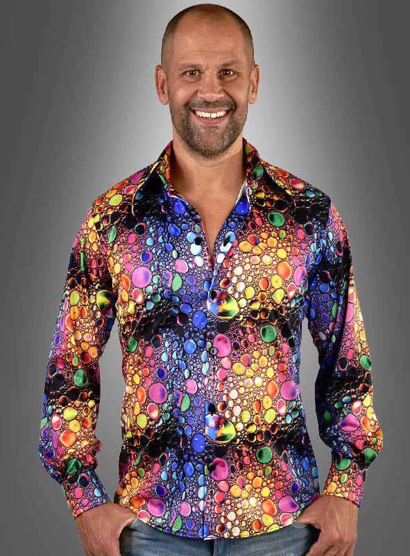 Ein Mann steht lächelnd vor einem grauen Hintergrund mit Farbverlauf und trägt das „Party Jersey Hemd Drops für Herren“ – ein farbenfrohes Hemd mit einem lebhaften Blasenmuster –, das sich perfekt für ausgelassene Feiern eignet.