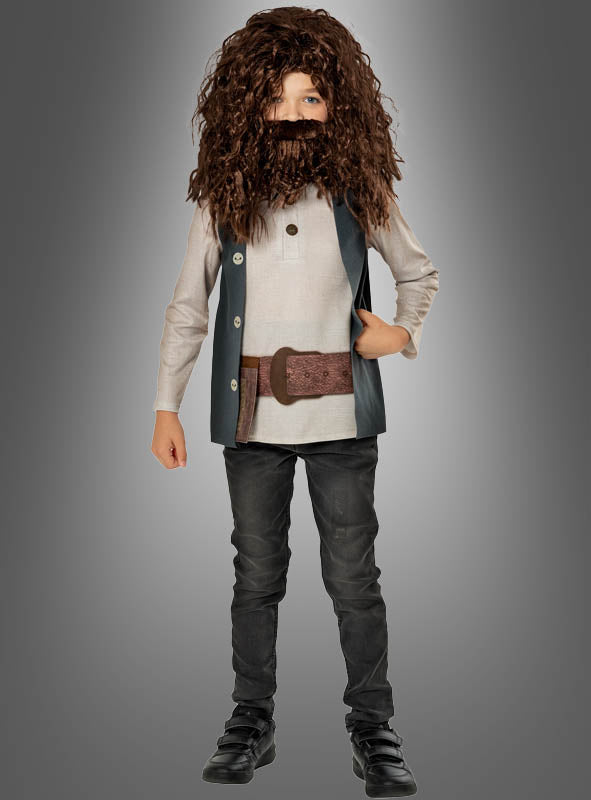 Ein Kind trägt das Deluxe-Hagrid-Kinderkostüm aus „Harry Potter“, bestehend aus einer großen braunen Perücke und einem Bart, einem beigen Hemd, einer dunklen Weste, einem breiten Gürtel, einer dunklen Hose und schwarzen Schuhen – damit ist es die ideale Wahl für jeden jungen „Harry Potter“-Fan, der einen authentischen Look sucht –, während es vor einem grauen Hintergrund mit Farbverlauf steht.