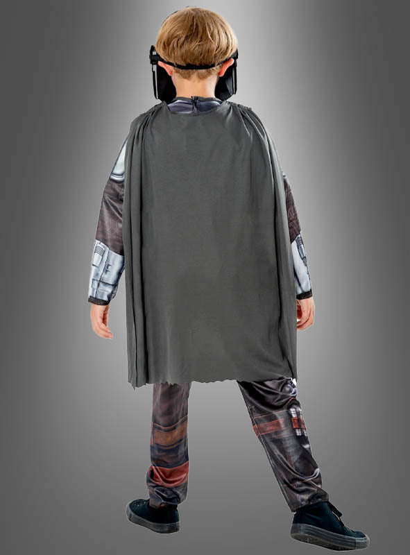Ein Kind, das das Mandalorianer-Kinderkostüm aus „Star Wars“ trägt – bestehend aus einem grauen Umhang, schwarzen Schuhen und einer schwarzen Maske –, steht mit dem Rücken zur Kamera vor einem grauen Hintergrund.