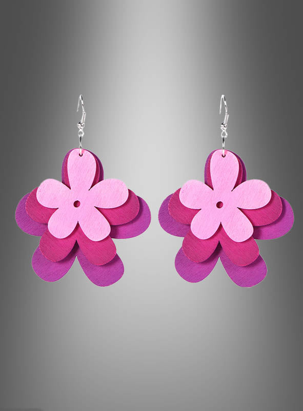 Ein Paar hängende Ohrringe in Form von übereinanderliegenden rosa und violetten Blumen, die an verspielte „Flower Hippie“-Ohrringe mit Holzblumen erinnern und vor einem grauen Hintergrund mit Farbverlauf präsentiert werden.