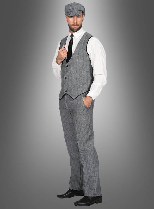 Ein Mann trägt das Herrenkostüm „Thomas“ im Stil der 20er Jahre, bestehend aus einer grauen Schiebermütze, einer passenden Weste und einer Hose im eleganten Fischgrätenmuster, einem weißen Hemd, einer schwarzen Krawatte und schwarzen Schuhen – ganz im authentischen „Peaky Blinders“-Stil. Mit einer Hand in der Tasche posiert er vor einem grau verlaufenden Hintergrund und verkörpert so perfekt das Flair der 20er Jahre.