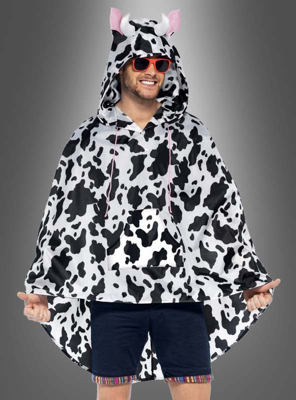 Eine Person, die den „Lustiger Kuh“-Regenponcho trägt – mit seinem schwarz-weißen Kuhmuster, den rosa Hörnern und Ohren –, kombiniert mit einer roten Sonnenbrille und Shorts, steht vor einem grauen Hintergrund und ist damit die ideale Wahl für originelle Regenbekleidung oder ein lustiges Karnevalskostüm.