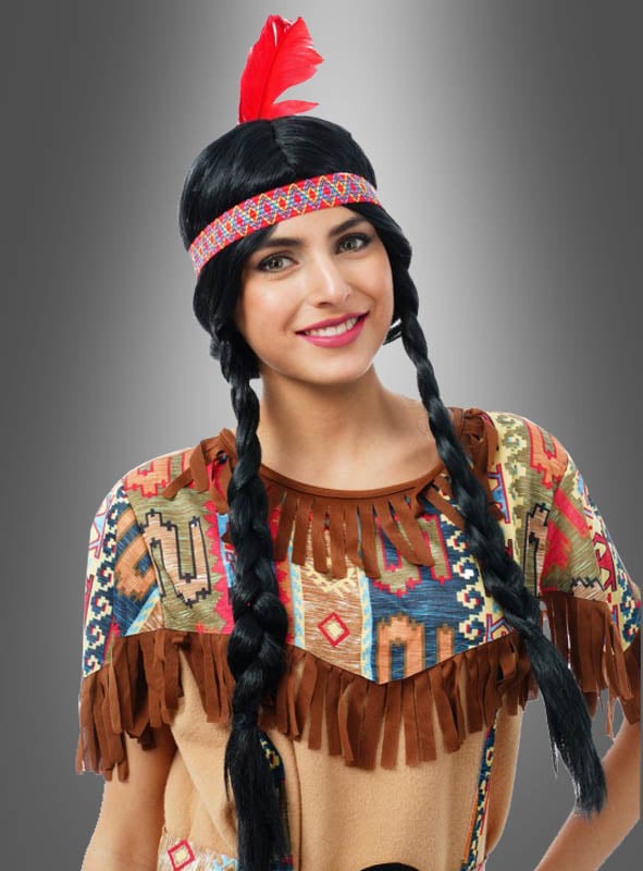 Eine Person trägt die „Indianerperücke für Erwachsene“ – eine geflochtene schwarze Perücke – sowie ein Stirnband mit einer roten Feder und ein gemustertes Kostüm mit Fransen und posiert vor einem grauen Hintergrund mit Farbverlauf.