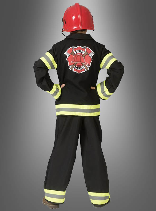 Ein Kind, das eine schwarze Feuerwehrmann-Uniform für Jungen mit reflektierenden Streifen und einen roten Feuerwehrhelm für Kinder trägt, steht mit dem Rücken zur Kamera und die Hände in die Hüften gestemmt.