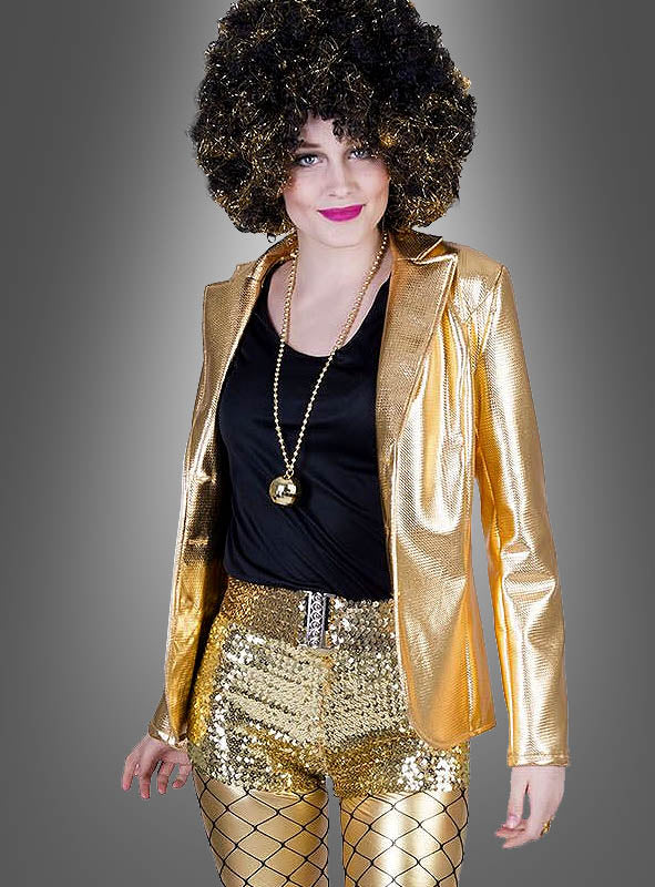 Eine Person trägt die „Glänzende Disco Jacke Damen“ in Gold, glänzende goldene Shorts, Netzstrümpfe, ein schwarzes Shirt, eine goldene Halskette und eine schwarze Lockenperücke und steht vor einem schlichten grauen Hintergrund.
