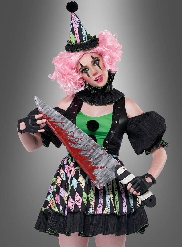 Eine Person, die das Damenkostüm „Verrückte Clownfrau Nicky“ trägt – komplett mit rosa Perücke und schwarzen Handschuhen –, steht lächelnd vor einem grauen Hintergrund mit Farbverlauf und hält ein großes, mit Kunstblut bespritztes Messer in der Hand.