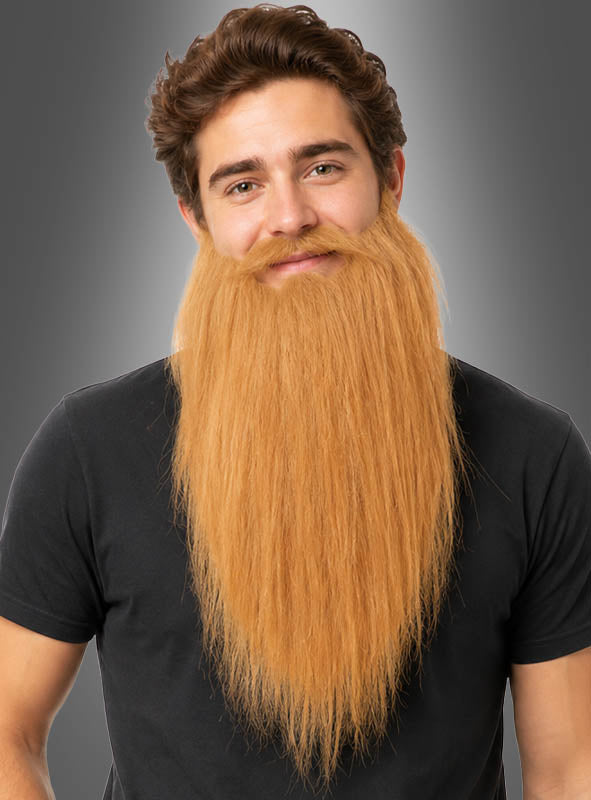 Ein Mann mit braunen Haaren und einem großen, langen, rotblonden Kunstbart („Langer Bart für Zauberer & Zwerge“) trägt ein schwarzes T-Shirt und lächelt vor einem grauen Hintergrund in die Kamera.