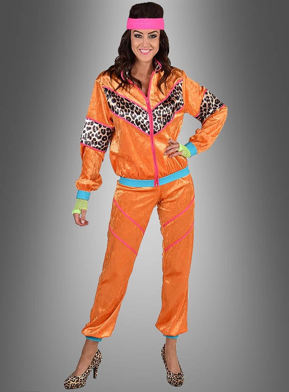 Eine Frau in einem XXL-Trainingsanzug im 80er-Jahre-Look in leuchtendem Orange mit Leopardenmuster-Details, kombiniert mit einem rosa Stirnband und passenden High Heels mit Leopardenmuster, steht lächelnd vor einem grauen Hintergrund – eine ideale Wahl für eine authentische 80er-Jahre-Party oder als auffälliges 80er-Jahre-Outfit.