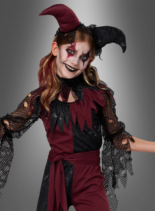 Ein Kind, das das Halloween-Narrenkostüm für Mädchen in Bordeauxrot und Schwarz trägt – mit auffälligem Gesichts-Make-up, schwarzem Lippenstift und einem Hut mit zwei Hörnern –, posiert vor einem grauen Hintergrund – ideal für jede Halloween-Feier mit Clownkostümen.