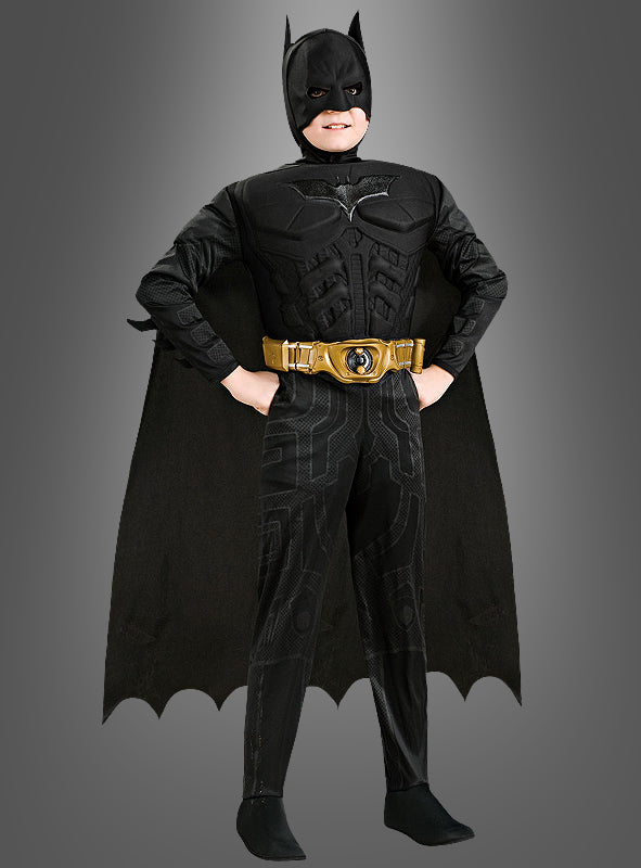 Ein Kind, das das „Batman-Kinderkostüm aus The Dark Knight“ trägt – bestehend aus einem gelben Werkzeuggürtel, einem schwarzen Umhang und einer Fledermausmaske –, steht vor einem grauen Hintergrund. Dieses beeindruckende Batman-Kinderkostüm aus The Dark Knight erweckt den kultigen Look zu Halloween zum Leben.