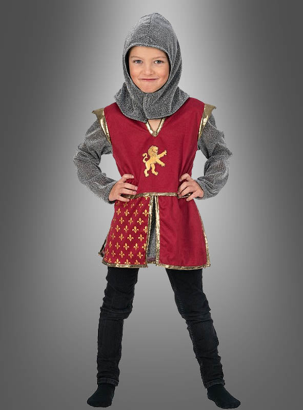 Ein Kind, das das Ritterkostüm „Leon Kinder Mittelalter“ trägt, steht vor einem einfarbigen Hintergrund mit Farbverlauf. Es ist mit einer roten Tunika mit goldenem Löwenwappen, einer schwarzen Hose und einer grauen Kapuze bekleidet.