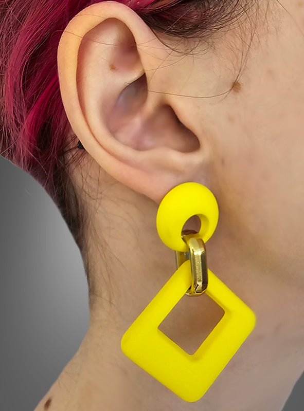 Nahaufnahme des Ohrs einer Person mit kurzen, rosafarbenen Haaren, die die „Retro-Ohrringe Stecker 60er Jahre“ trägt – markante, geometrische Ohrringe in leuchtendem Neongelb mit einem goldenen Verbindungsstück und einem quadratischen Anhänger, inspiriert vom ikonischen Stil der 1960er Jahre.