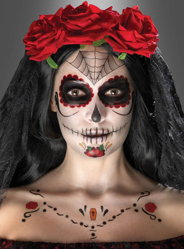 Eine Person mit „Tag der Toten“-Gesichtsbemalung, einer Krone aus roten Rosen, einem schwarzen Schleier und aufwendigen Mustern im Gesicht und auf der Brust blickt in die Kamera – dieser auffällige Look wurde mit dem „Tag der Toten“-Make-up-Tattoo-Set kreiert, um einen authentischen Sugar-Skull-Make-up-Effekt zu erzielen.