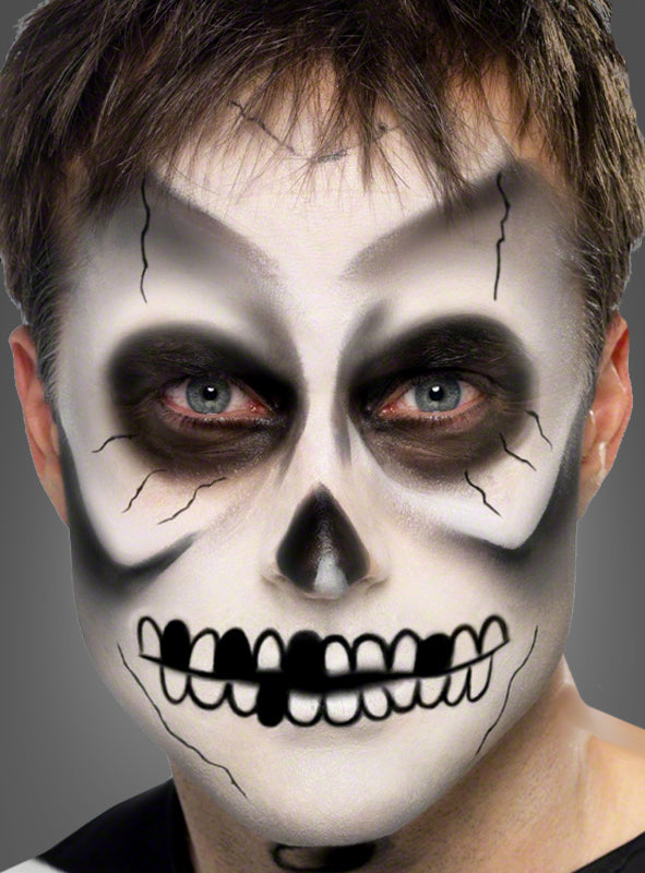 Eine Person mit einem realistisch wirkenden Schädel-Facepaint-Look, der mit dem „Skelett Make-up Schmink-Set schwarz-weiß“ gestaltet wurde, mit schwarz-weißen Schattierungen um Augen, Nase und Mund sowie dunklen, rissartigen Linien vor einem neutralen Hintergrund.