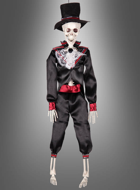 Die 42 cm große „Tag der Toten“-Voodoo-Puppe – erhältlich als Braut oder Bräutigam – zeigt eine Skelettfigur in einem schwarzen Anzug mit roten Akzenten und einem Zylinder, die vor einem grauen Hintergrund mit Farbverlauf posiert. Diese auffällige Dekoration eignet sich perfekt, um mexikanisches Halloween zu feiern oder die Tradition des Skelett-Brautpaares zu würdigen.