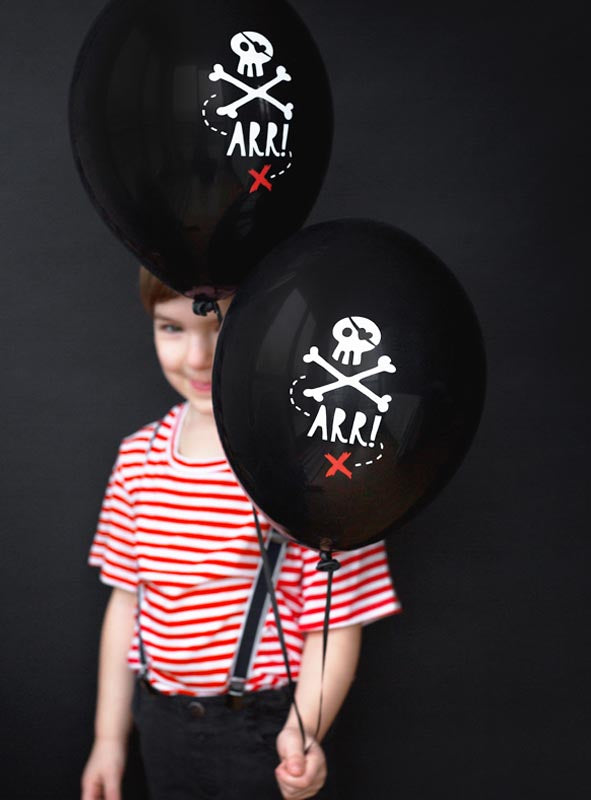 Ein Kind in einem rot-weiß gestreiften Hemd hält zwei schwarze Luftballons mit Totenkopf (30 cm) in der Hand, die jeweils ein Totenkopf-Motiv mit der Aufschrift „ARR!“ auf schwarzem Hintergrund zeigen.