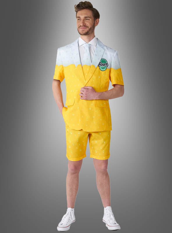 Ein Mann im „Sommerlicher Bieranzug“ – einem gelb-weißen Outfit mit Shorts, die einem Bierglas nachempfunden sind – steht vor einem grauen Hintergrund mit Farbverlauf und präsentiert damit das perfekte Sommeroutfit für jeden Bierliebhaber.