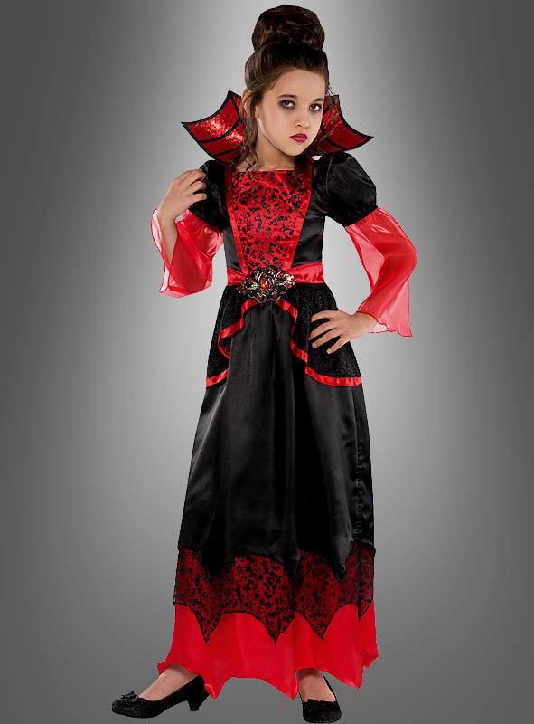 Ein Mädchen, das das auffällige „Vampirgräfin“-Kostüm für Mädchen trägt – ein elegantes rot-schwarzes Vampir-Kleid mit hohem Kragen –, steht vor einem grauen Hintergrund, was dieses Halloween-Kostüm zu einem echten Highlight für Mädchen macht.