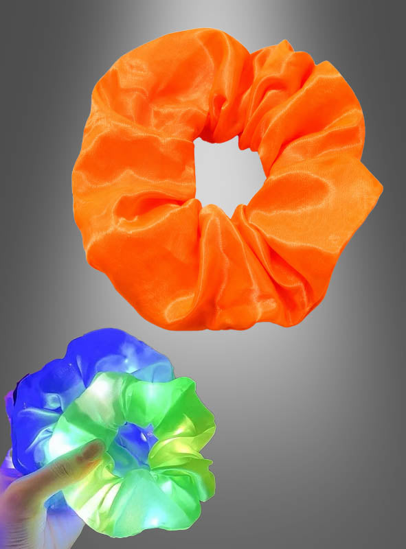 Ein orangefarbenes Scrunchie-Haargummi mit LED ist über einer Hand abgebildet, die das leuchtende Scrunchie hält, das vor einem grauen Hintergrund mit blauen, grünen und weißen LEDs leuchtet – ein echter Blickfang unter den leuchtenden Haarschmuckstücken.