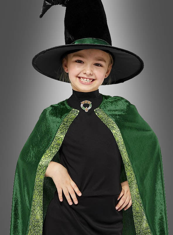 Ein junges Mädchen lächelt, es trägt einen schwarzen Hexenhut und einen grünen Samtumhang mit goldener Borte über einem schwarzen Shirt und verkörpert damit perfekt den magischen Geist des Professor-McGonagall-Kostüms für Kinder.
