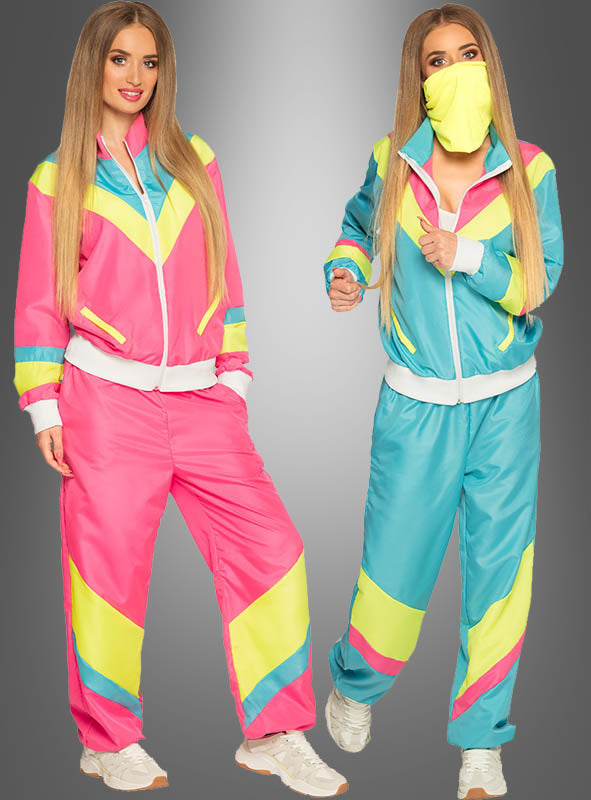 Zwei Frauen präsentieren den „Neon Trainingsanzug 80er Jahre“ und tragen dazu passende Retro-Trainingsanzüge, die mit kräftigen Farben wie Pink, Blau, Gelb und Weiß den pulsierenden Geist der 80er Jahre einfangen. Eine von ihnen rundet ihren Look mit einer gelben Gesichtsmaske ab. Beide posieren selbstbewusst vor einem grauen Hintergrund mit Farbverlauf und strahlen den authentischen Retro-Jogginganzug-Stil aus.