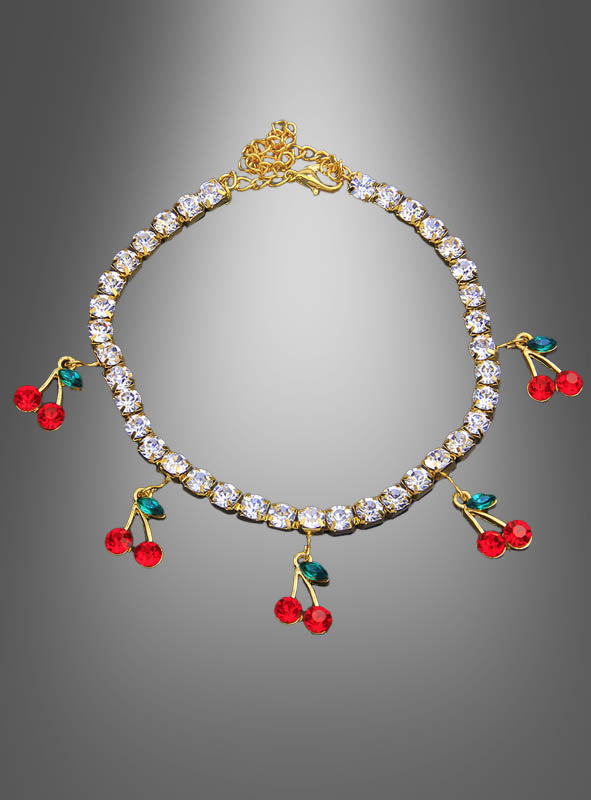 Strass-Armband mit Kirschen in Gold, verziert mit klaren Steinen und fünf roten Kirsch-Anhängern, die jeweils mit zwei grünen Blättern geschmückt sind, vor einem grau verlaufenden Hintergrund.