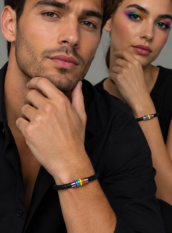 Ein Mann und eine Frau tragen beide schwarze Shirts und dazu passende schwarze geflochtene Armbänder, die mit bunten Perlen verziert sind, und posieren mit den Händen nahe am Gesicht. Zu ihren Accessoires gehört das Unisex-Armband „Rainbow“, das ihrem aufeinander abgestimmten Look einen Hauch von modernem Stil verleiht.