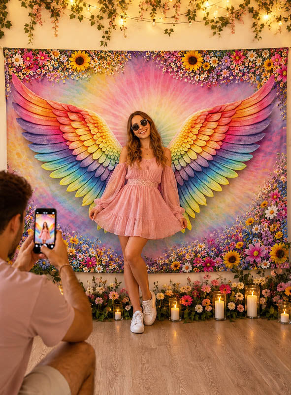 Eine Frau in einem rosa Kleid posiert vor dem „Bunte Flügel“-Fotopunkt (170 x 200 cm), während jemand ein Foto von ihr macht. Die Kulisse ist mit Blumen, Kerzen und Lichterketten geschmückt und bildet so die perfekte Partydekoration für unvergessliche Erinnerungen an der Fotowand.