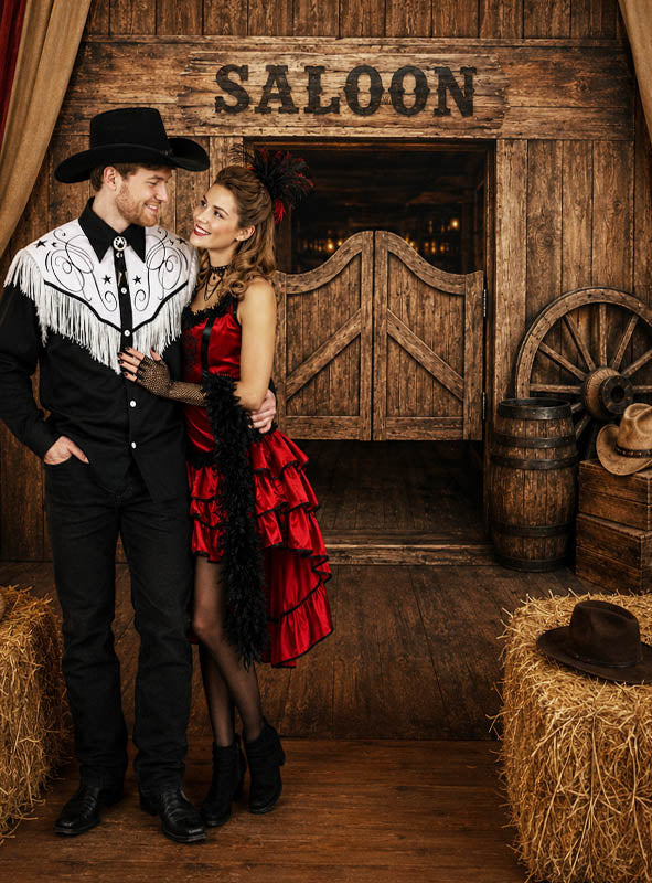 Ein Mann in Cowboy-Kleidung und eine Frau in einem roten Saloon-Kleid stehen gemeinsam vor dem „Western Saloon Fotohintergrund XXL 170 x 220 cm“, der einen mit Heuballen, Fässern und klassischen Western-Requisiten geschmückten Saloon-Eingang aus Holz zeigt – die perfekte Kulisse für jede Themenveranstaltung.